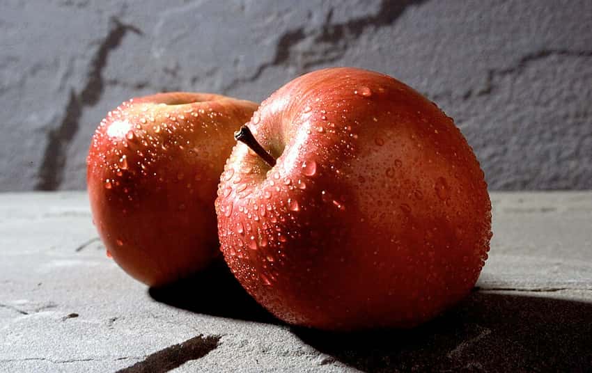 Two ripe red Fuji apples with water droplets.
