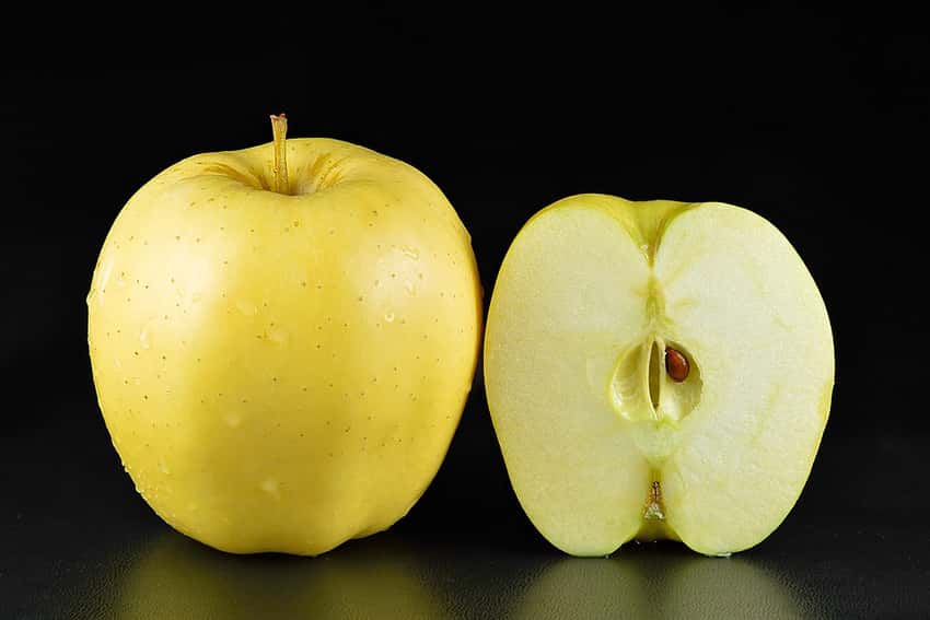 Whole Golden Delicious apple beside a cut half.