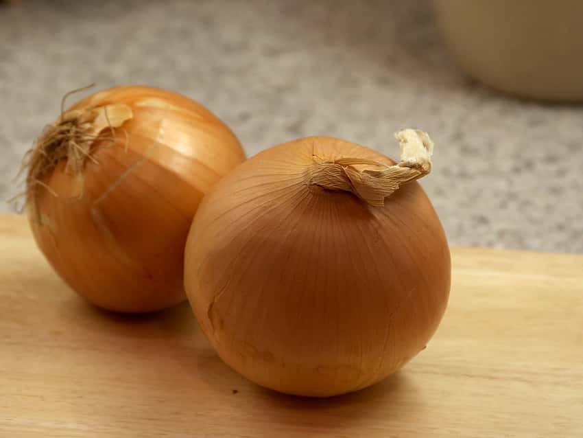Two golden-brown yellow onion bulbs on a cutting board.